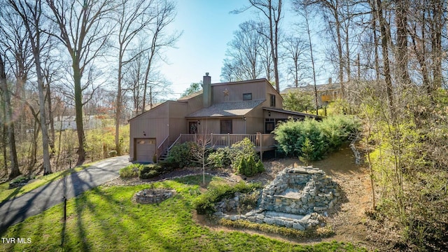 back of property with a deck, aphalt driveway, a garage, and a chimney