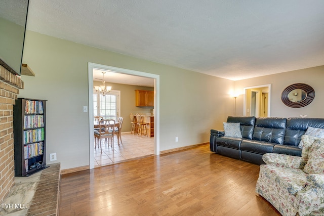 living area featuring a fireplace, baseboards, a chandelier, and light wood-style flooring