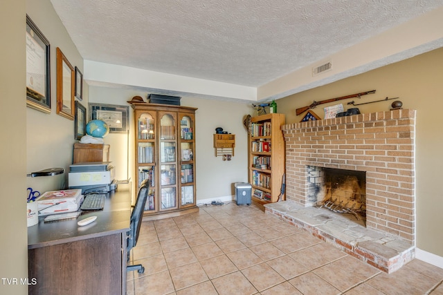 office area with a brick fireplace, a textured ceiling, visible vents, and light tile patterned floors