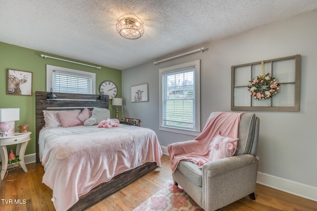 bedroom with multiple windows, wood finished floors, baseboards, and a textured ceiling