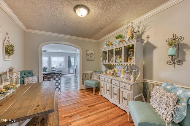 interior space with a textured ceiling, light wood-style flooring, arched walkways, and ornamental molding