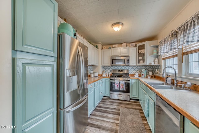 kitchen with light countertops, decorative backsplash, wood finished floors, stainless steel appliances, and a sink