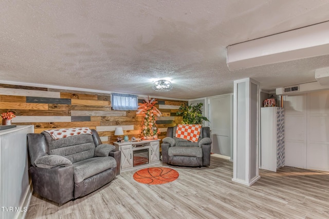 living area with wooden walls, visible vents, light wood-type flooring, and a textured ceiling
