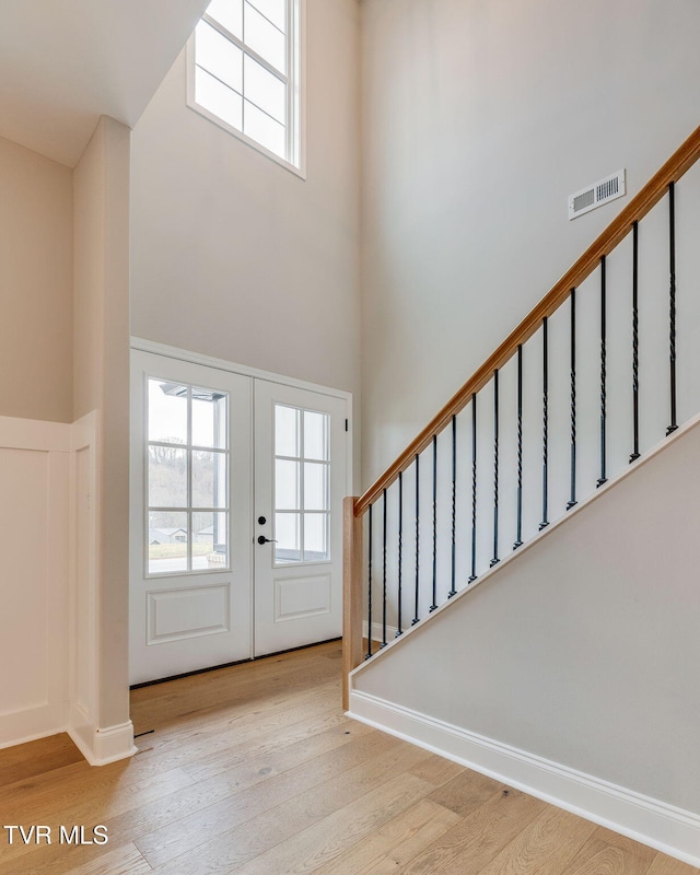 entrance foyer with visible vents, wood finished floors, french doors, stairway, and a high ceiling