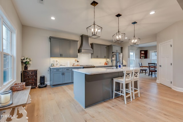 kitchen with a sink, decorative backsplash, light countertops, custom range hood, and light wood-type flooring