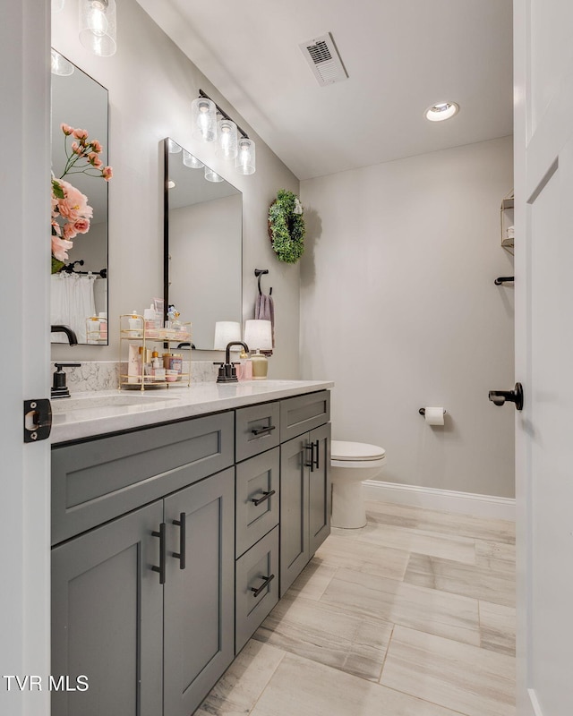 full bath featuring baseboards, visible vents, double vanity, a sink, and toilet
