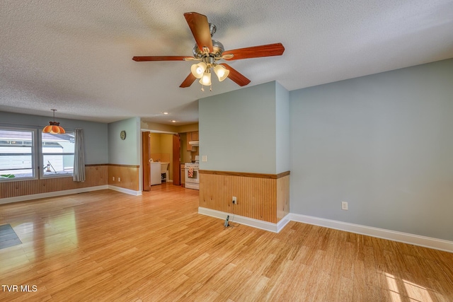 empty room featuring light wood-type flooring, baseboards, wainscoting, a textured ceiling, and ceiling fan