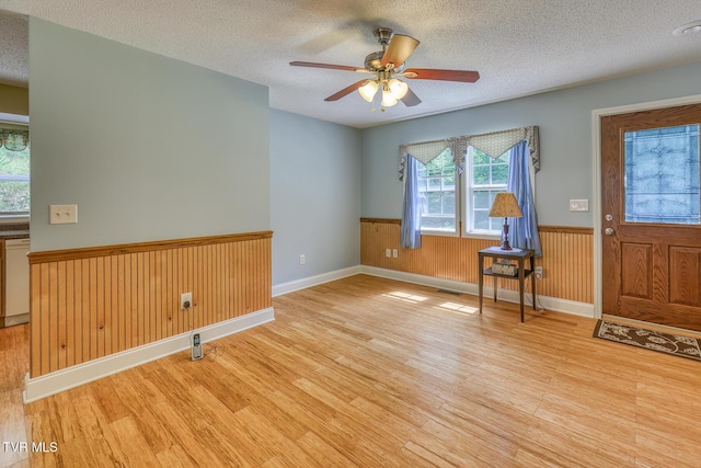 entrance foyer featuring wainscoting, light wood finished floors, and a textured ceiling
