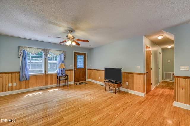 living room with light wood-type flooring, a textured ceiling, a wainscoted wall, and a ceiling fan