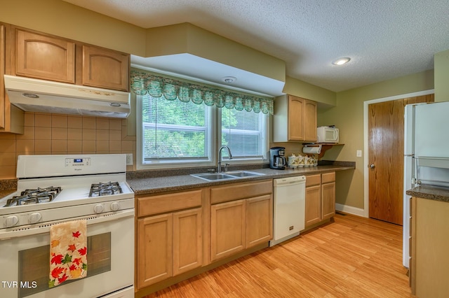 kitchen featuring a sink, light wood-type flooring, dark countertops, white appliances, and under cabinet range hood