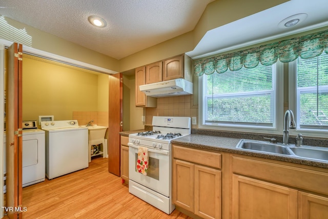 kitchen featuring dark countertops, a sink, separate washer and dryer, under cabinet range hood, and white range with gas cooktop