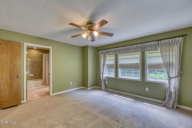 unfurnished bedroom featuring a ceiling fan, a textured ceiling, ensuite bathroom, carpet floors, and baseboards