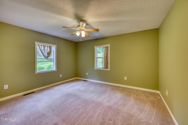 carpeted empty room with a textured ceiling, visible vents, a ceiling fan, and baseboards