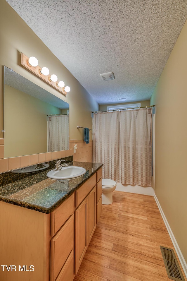 bathroom with toilet, wood finished floors, visible vents, and a textured ceiling