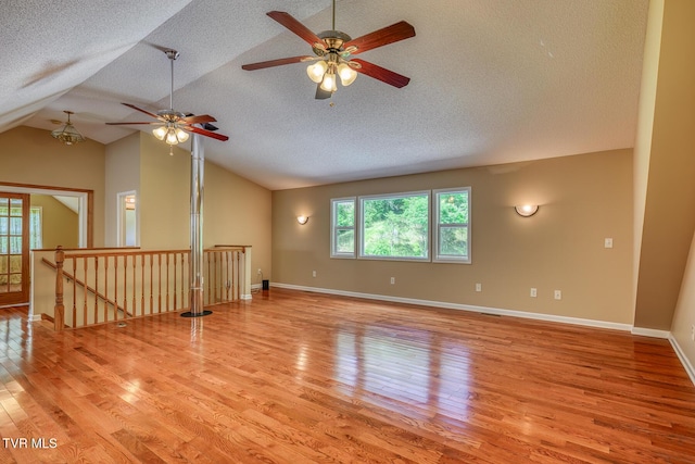 interior space with vaulted ceiling, light wood-style floors, baseboards, a textured ceiling, and ceiling fan