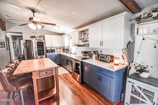 kitchen with a ceiling fan, open shelves, appliances with stainless steel finishes, decorative backsplash, and vaulted ceiling