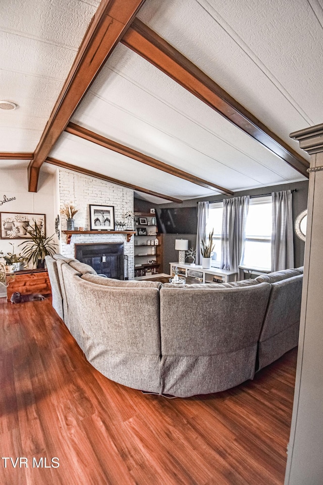 living area with a textured ceiling, vaulted ceiling with beams, wood finished floors, and a fireplace