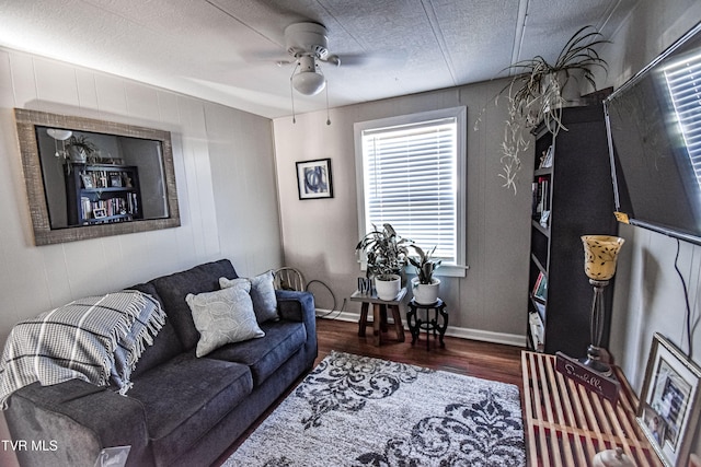 living room featuring baseboards, a textured ceiling, a ceiling fan, and wood finished floors