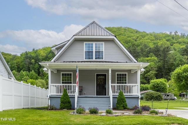 view of front of house featuring fence, a forest view, covered porch, and a front yard