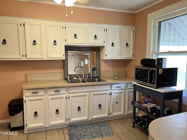 kitchen with stainless steel microwave, light countertops, a sink, and white cabinetry