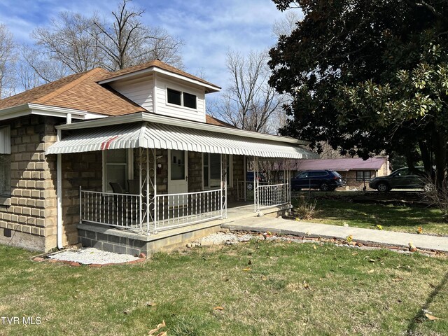 view of front of house featuring covered porch, stone siding, a front yard, and roof with shingles
