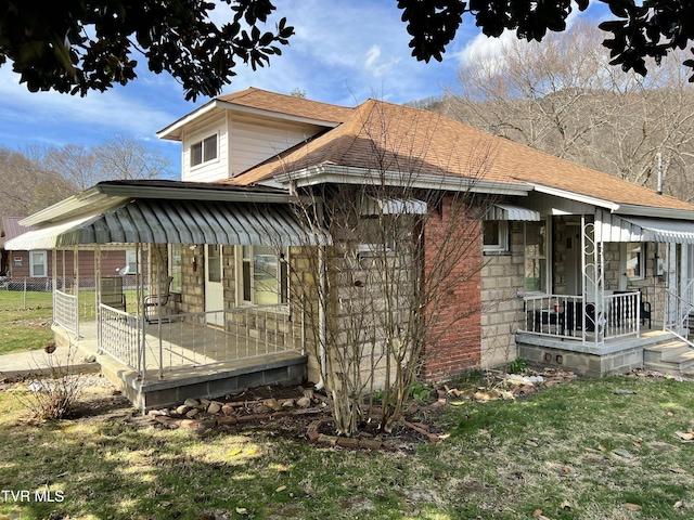 view of side of property with stone siding, fence, covered porch, a shingled roof, and a yard