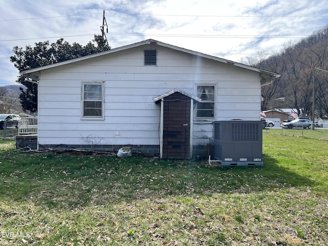 rear view of house featuring fence, central AC, and a yard