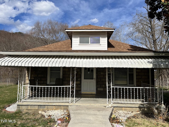 view of front of house with covered porch, stone siding, and roof with shingles