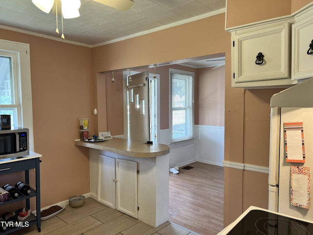 kitchen with light wood-type flooring, stainless steel microwave, ornamental molding, ceiling fan, and a peninsula