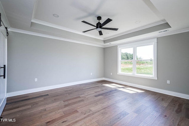 unfurnished room featuring a tray ceiling, ceiling fan, crown molding, a barn door, and wood finished floors