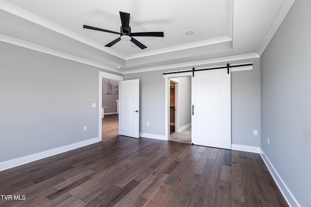 unfurnished bedroom with a raised ceiling, crown molding, dark wood-type flooring, a barn door, and baseboards