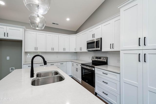 kitchen with appliances with stainless steel finishes, a sink, light countertops, backsplash, and lofted ceiling