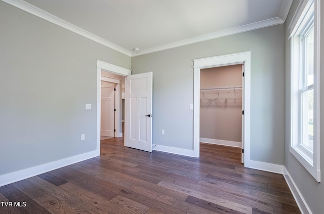 unfurnished bedroom featuring crown molding, dark wood finished floors, baseboards, and a spacious closet