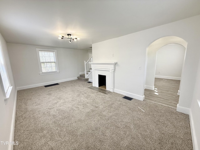 unfurnished living room with arched walkways, visible vents, baseboards, and carpet