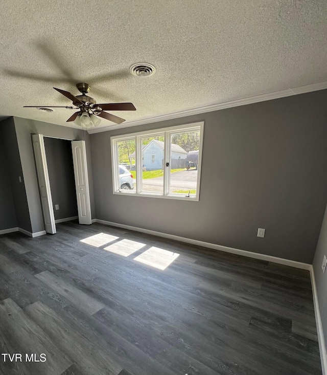 unfurnished bedroom featuring dark wood-style flooring, baseboards, ornamental molding, a textured ceiling, and visible vents