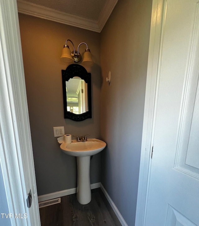 bathroom featuring baseboards, ornamental molding, visible vents, a sink, and wood finished floors
