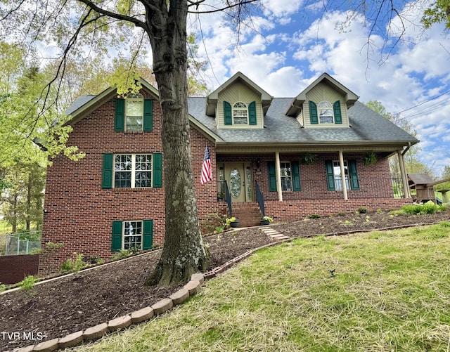 view of front of property featuring a porch, a shingled roof, brick siding, and a front yard
