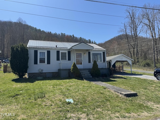 view of front of property with a wooded view, a front yard, driveway, and metal roof