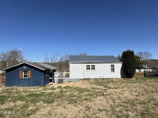 rear view of house with an outdoor structure, fence, a wooden deck, metal roof, and a lawn