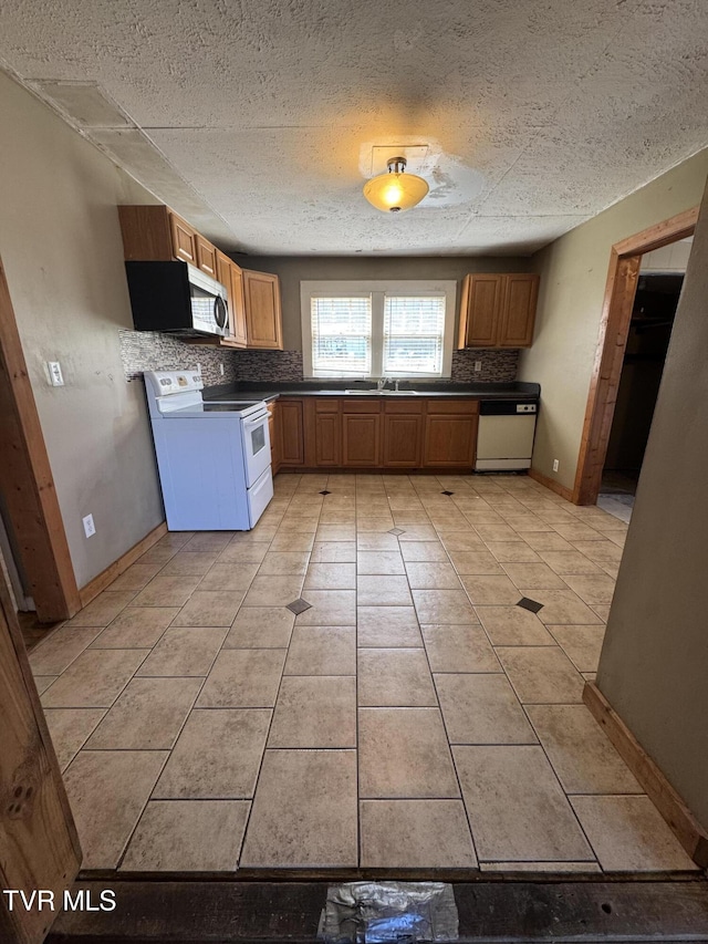 kitchen with light tile patterned flooring, white appliances, brown cabinets, a sink, and backsplash
