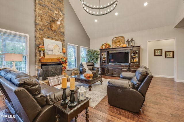 living room with wood-type flooring, a stone fireplace, high vaulted ceiling, and a chandelier