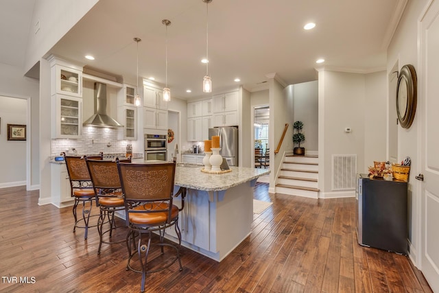 kitchen featuring decorative backsplash, visible vents, stainless steel appliances, white cabinetry, and wall chimney range hood