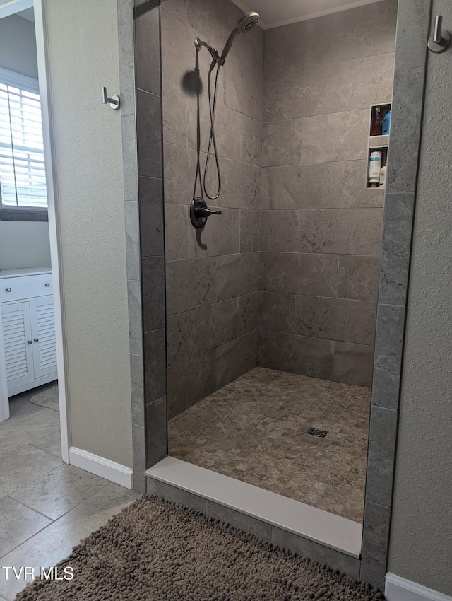 bathroom with a tile shower, baseboards, and tile patterned floors