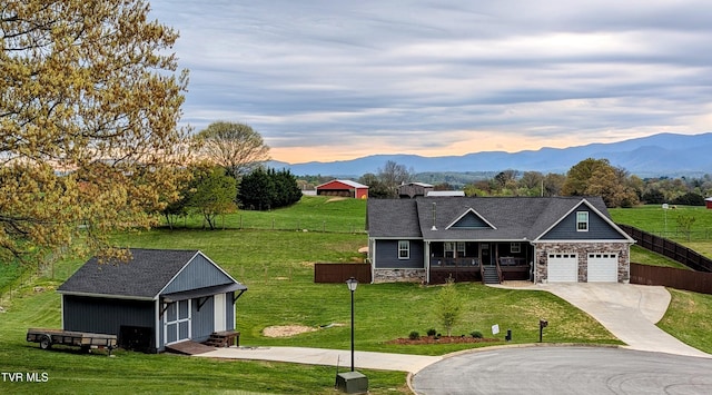 view of front facade featuring concrete driveway, covered porch, stone siding, a lawn, and a mountain view