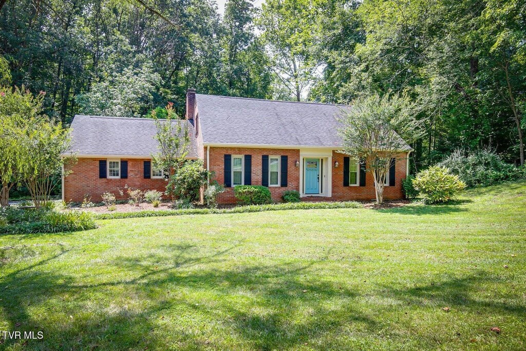 view of front of property featuring brick siding, a chimney, a shingled roof, and a front yard