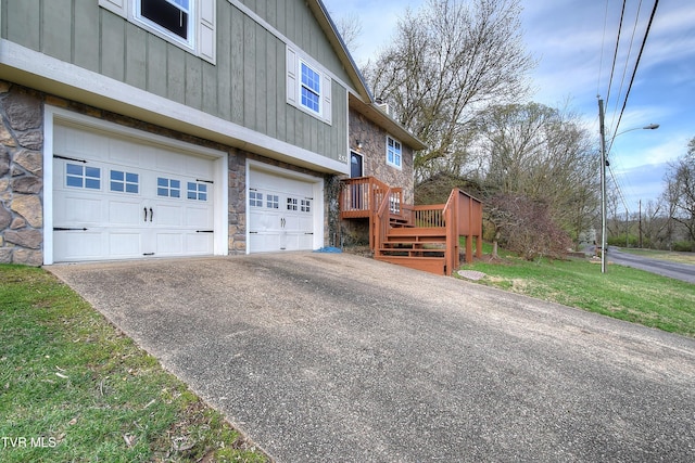 view of side of property with stone siding, board and batten siding, aphalt driveway, a lawn, and a garage