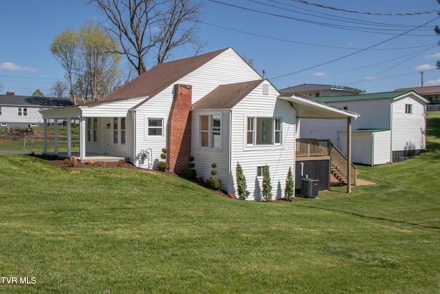 back of house featuring roof with shingles, central air condition unit, stairway, a lawn, and an outdoor structure