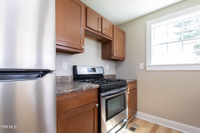kitchen with brown cabinets, dark countertops, appliances with stainless steel finishes, light wood finished floors, and visible vents