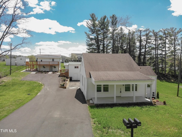 view of front of home featuring a front lawn, fence, covered porch, roof with shingles, and driveway
