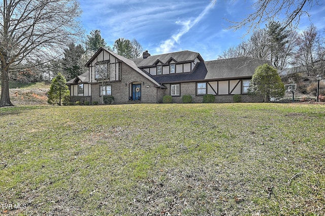tudor house featuring a chimney, brick siding, and a front yard